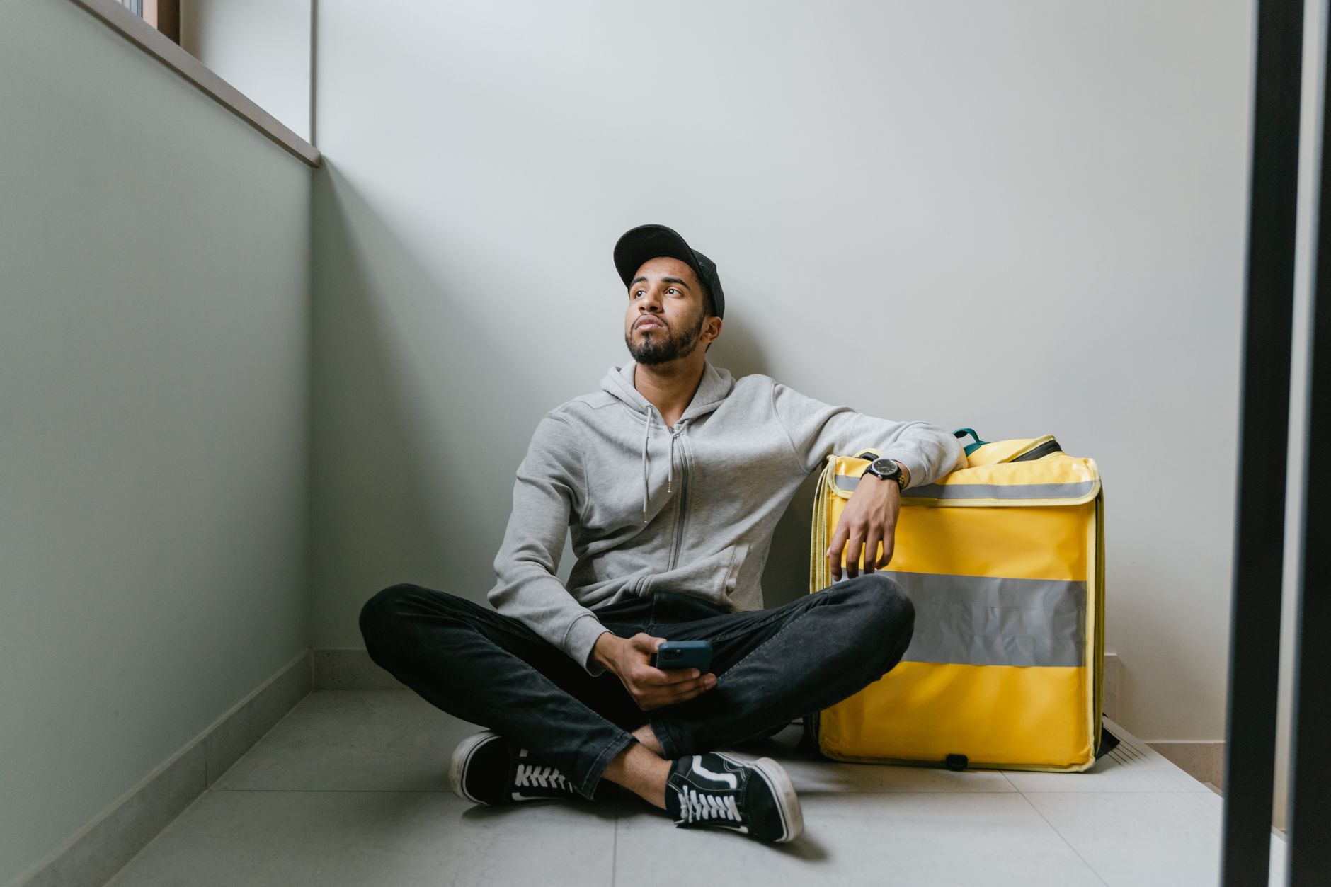 Entregador sentado no chão com bolsa térmica, em pausa