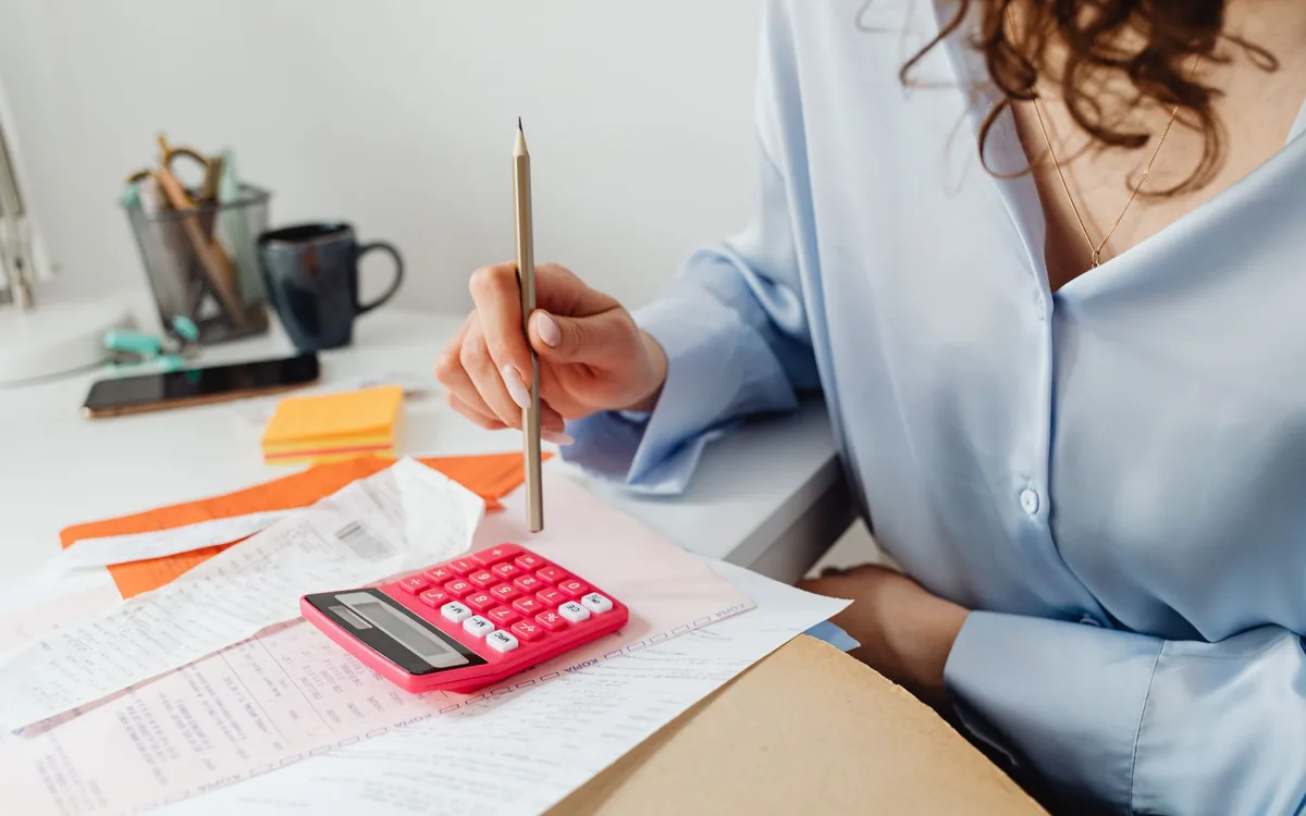 Pessoa calculando o rendimento mensal com calculadora e papéis na mesa