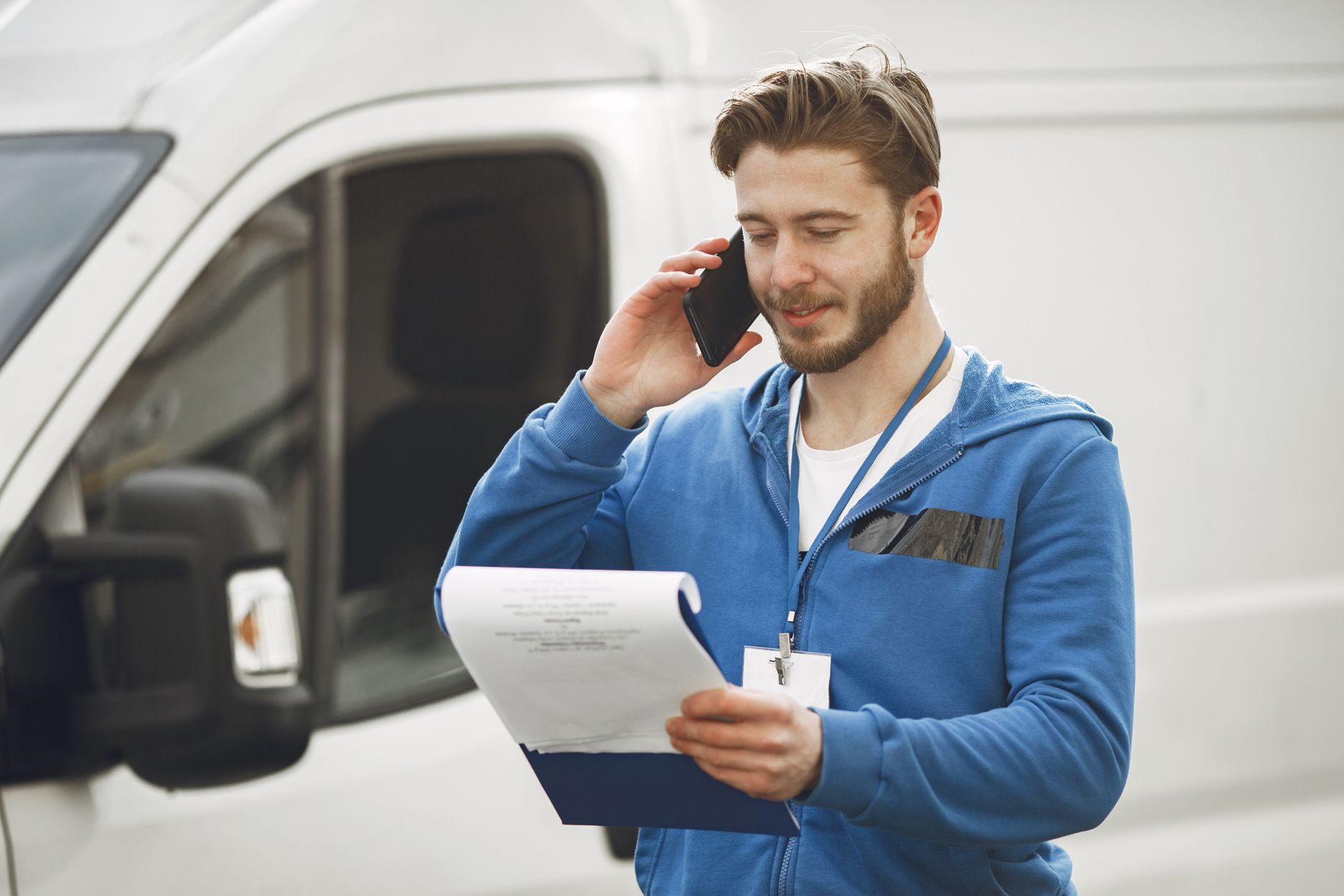 Motorista de entrega conferindo celular ao lado da van