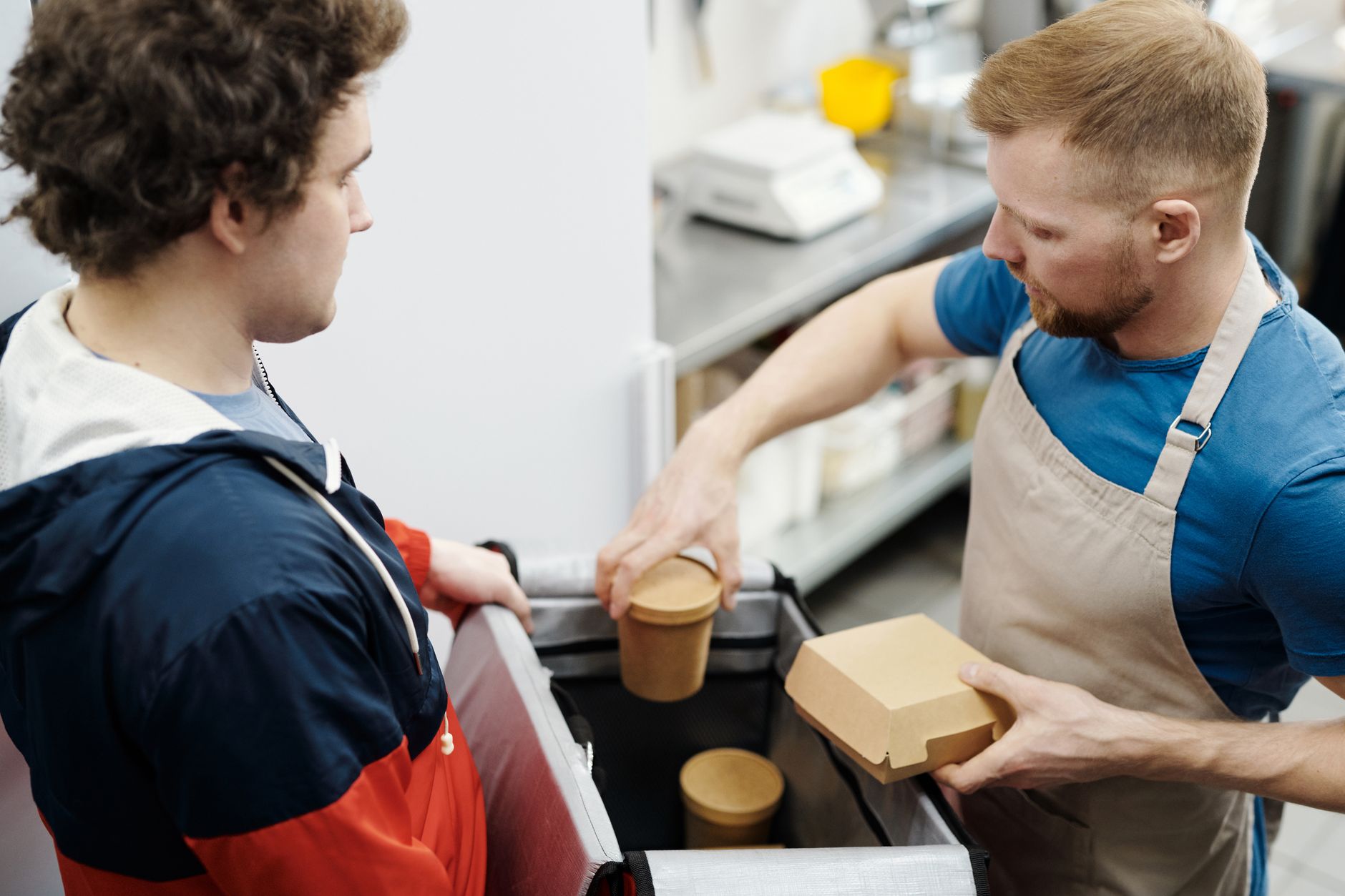 Entregador recebendo pedido de funcionário na cozinha do restaurante