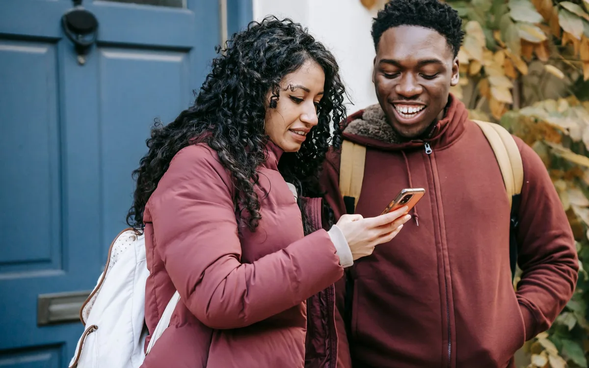 Duas pessoas olhando juntas para a tela de um celular, uma indicando algo pra outra