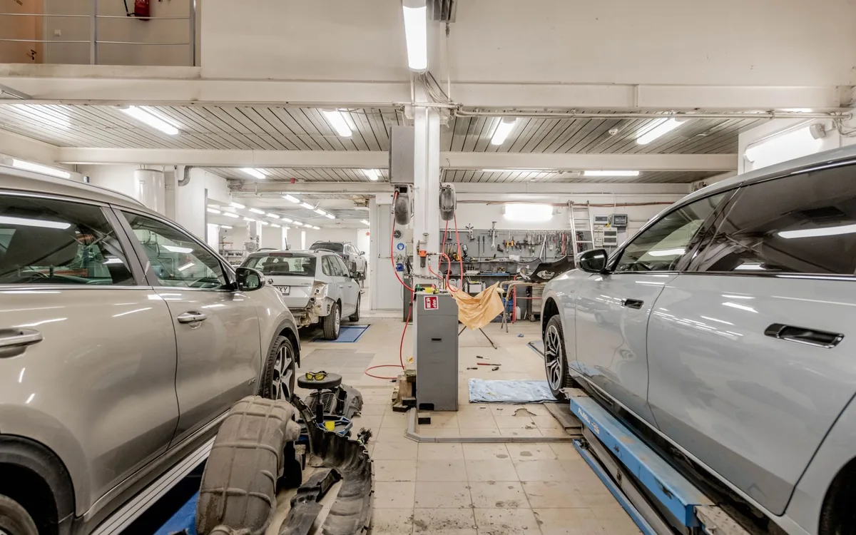 Oficina mecânica com carros em atendimento — status do serviço e ofertas na TV da sala de espera