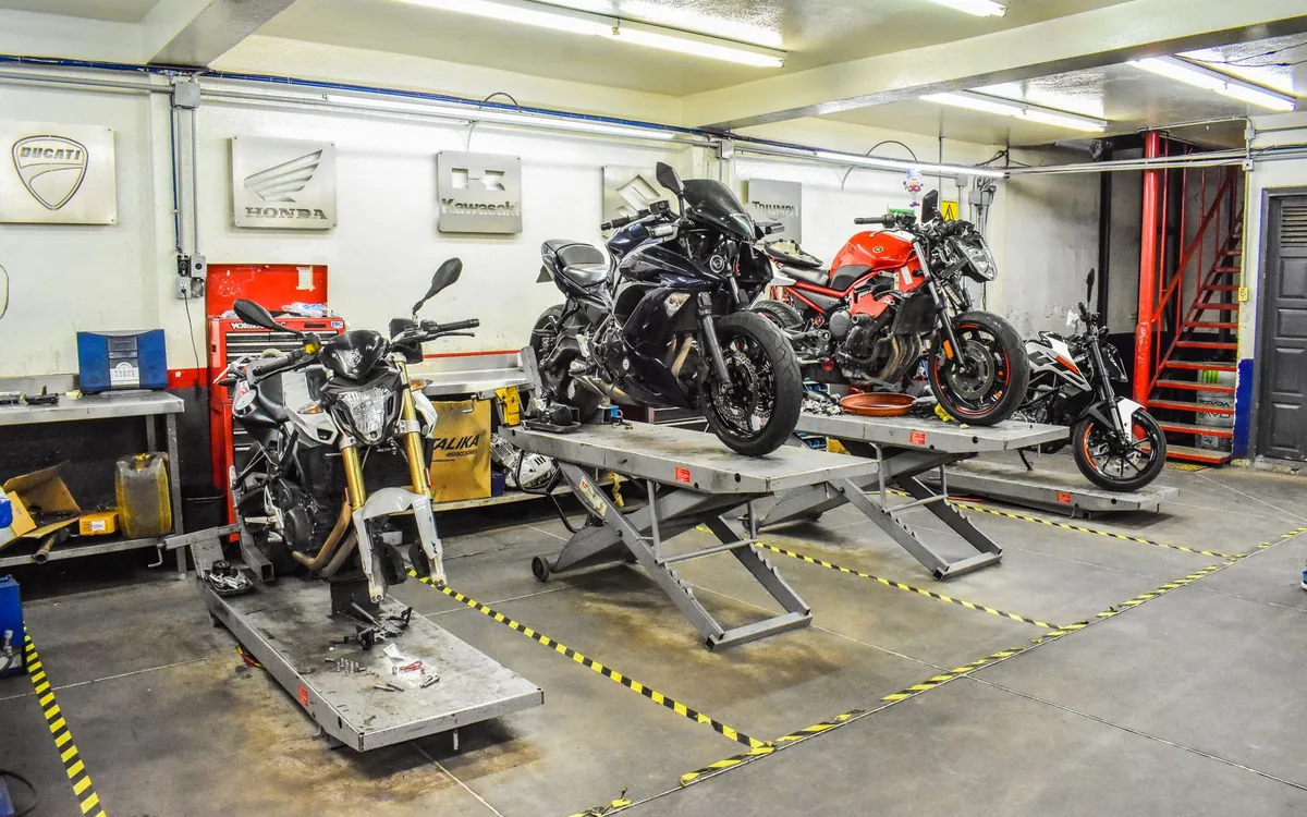 Oficina de moto com motos em manutenção — vitrine de acessório e status na TV da oficina